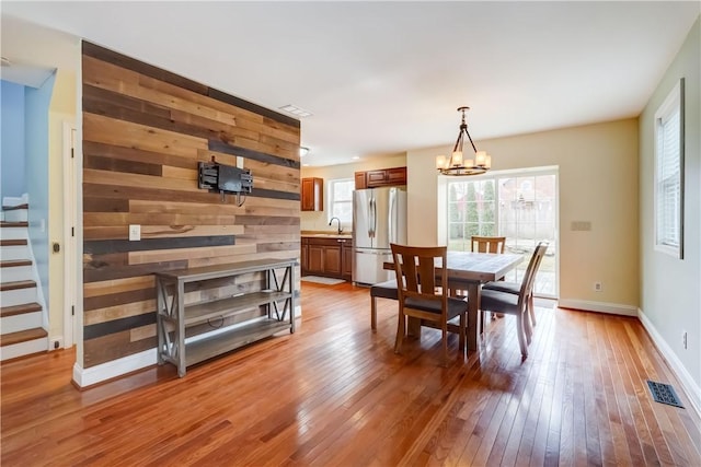 dining area with stairway, wooden walls, baseboards, an inviting chandelier, and light wood-style floors