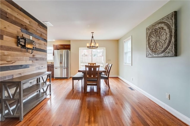 dining area with visible vents, wooden walls, baseboards, a chandelier, and wood-type flooring