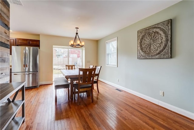 dining area with a notable chandelier, visible vents, baseboards, and hardwood / wood-style flooring