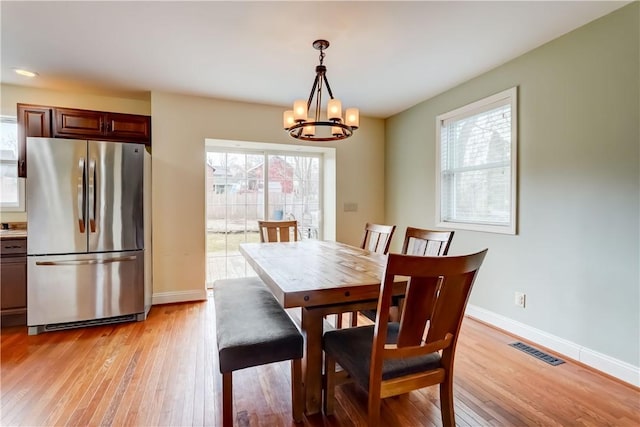 dining area with light wood-type flooring, visible vents, baseboards, and an inviting chandelier