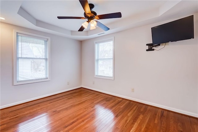 empty room with a tray ceiling, baseboards, visible vents, and wood-type flooring