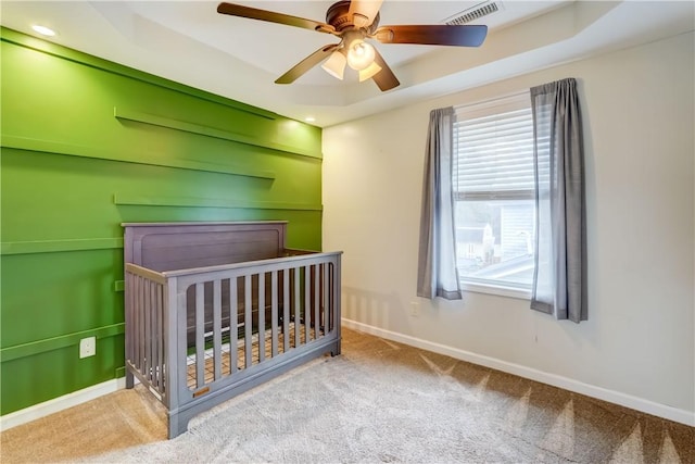 carpeted bedroom featuring visible vents, a raised ceiling, and baseboards