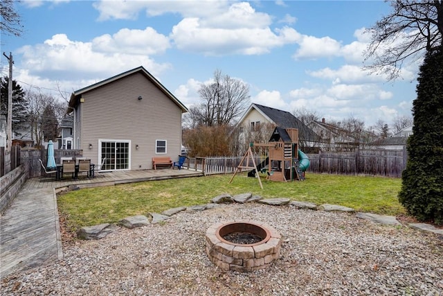 back of house featuring a playground, an outdoor fire pit, a wooden deck, a yard, and a fenced backyard