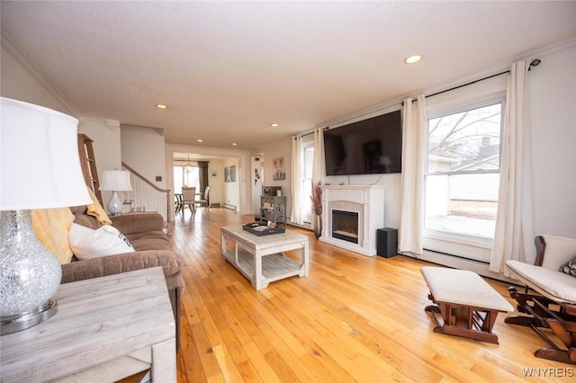 living room featuring light wood finished floors, recessed lighting, a fireplace, stairs, and a baseboard heating unit