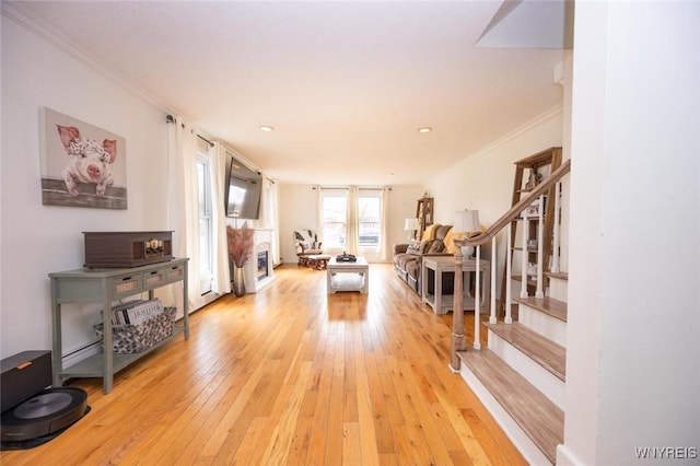 living area featuring stairway, light wood-style flooring, a fireplace, and ornamental molding