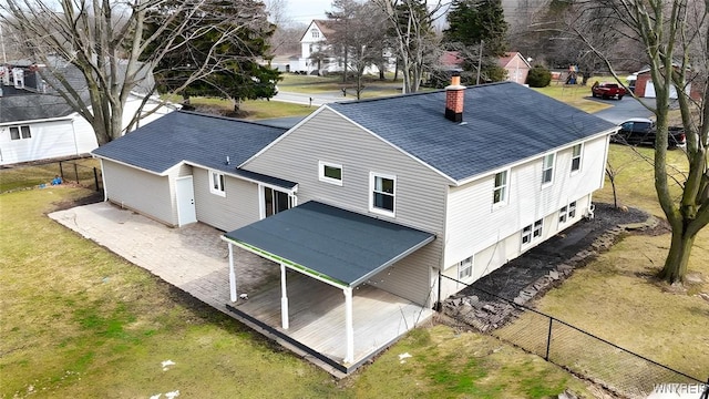 back of property featuring a patio, fence, a yard, roof with shingles, and a chimney