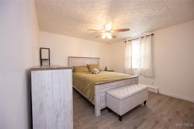 bedroom featuring ceiling fan, an ornate ceiling, baseboards, and wood finished floors