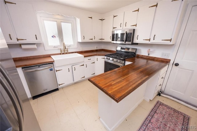 kitchen with wooden counters, light floors, appliances with stainless steel finishes, white cabinets, and a sink