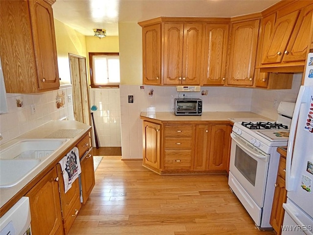 kitchen featuring light wood finished floors, light countertops, brown cabinetry, white appliances, and a sink