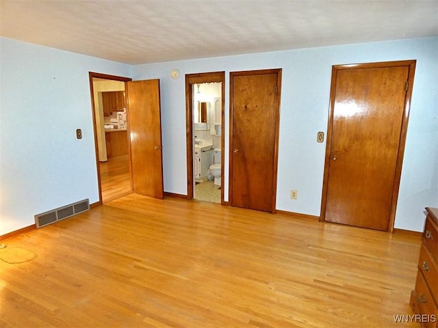 unfurnished bedroom with light wood-type flooring, visible vents, baseboards, and ensuite bath