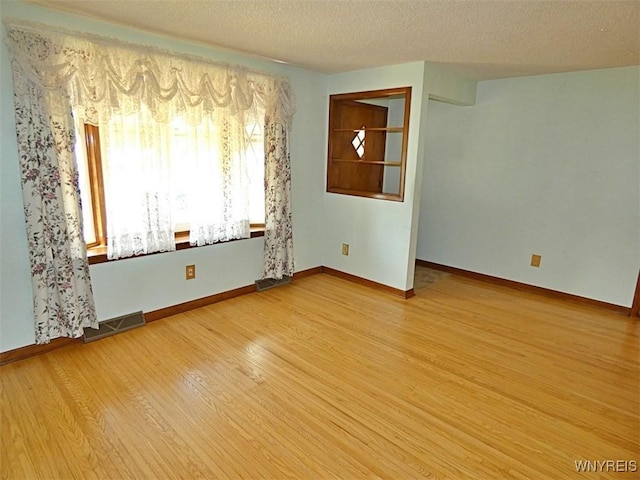 unfurnished room with visible vents, baseboards, a textured ceiling, and light wood finished floors