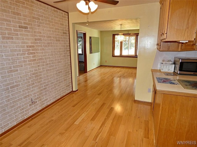 kitchen with stainless steel microwave, brick wall, baseboards, light countertops, and light wood-style floors