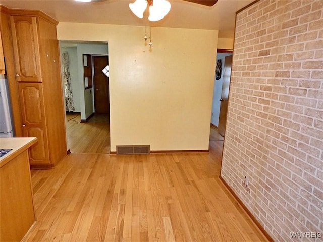 unfurnished dining area featuring light wood-type flooring, visible vents, brick wall, and a ceiling fan