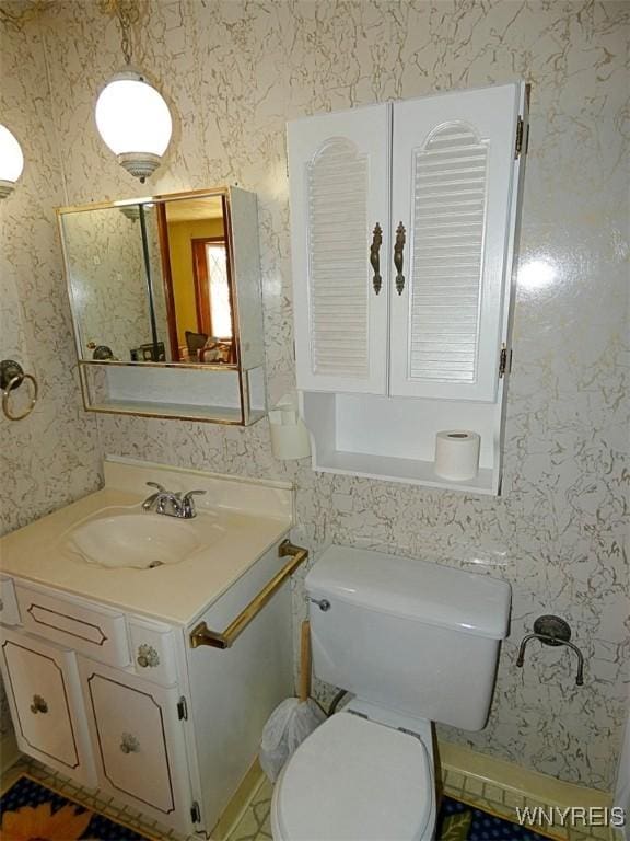 half bathroom featuring toilet, wallpapered walls, and vanity