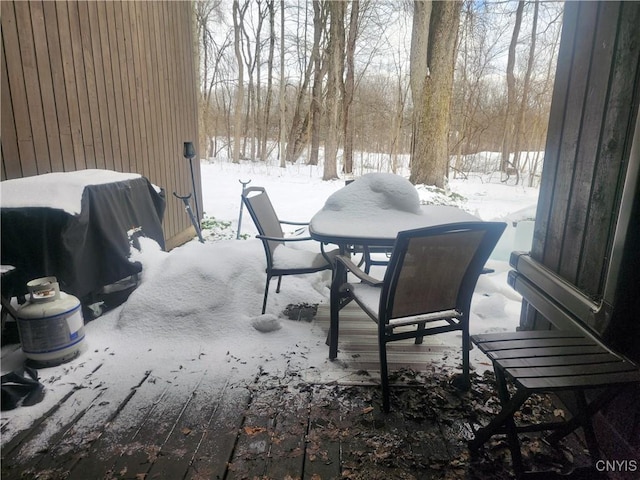 snow covered patio with outdoor dining area and a grill