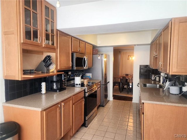 kitchen with a sink, backsplash, stainless steel appliances, light tile patterned floors, and glass insert cabinets