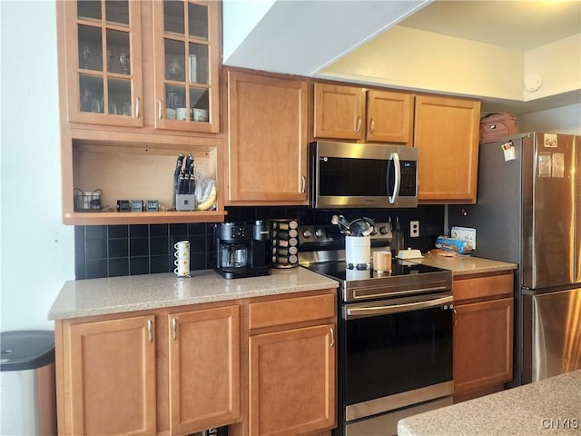 kitchen with glass insert cabinets, backsplash, appliances with stainless steel finishes, and light countertops