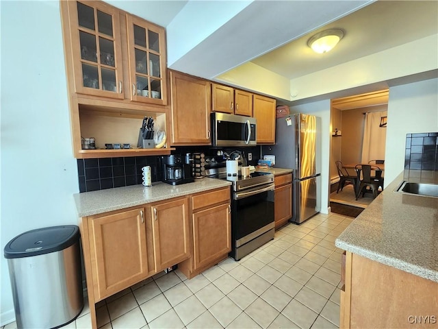 kitchen with light tile patterned flooring, a sink, stainless steel appliances, glass insert cabinets, and backsplash