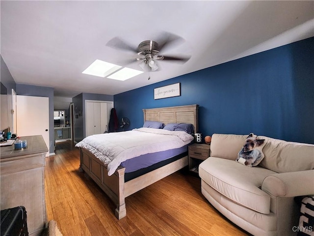 bedroom featuring a ceiling fan, a skylight, light wood-style flooring, and a closet