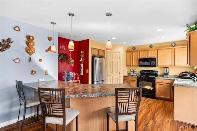 kitchen featuring black appliances, a sink, a kitchen breakfast bar, dark wood-style floors, and a peninsula