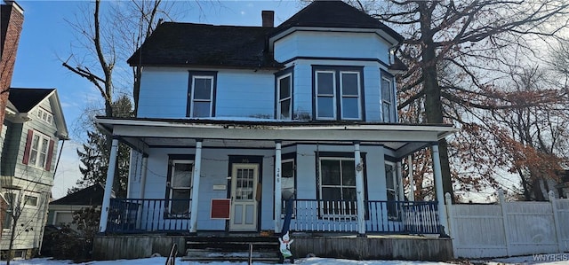 view of front of house featuring a porch, a chimney, and fence