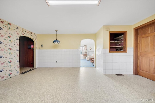 spare room with visible vents, arched walkways, tile walls, and wainscoting