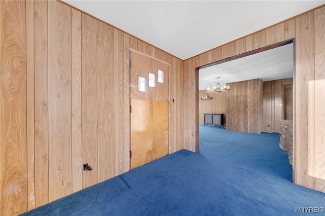 carpeted spare room with a chandelier and wooden walls