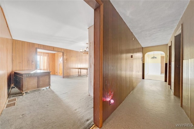 corridor featuring wooden walls, carpet, visible vents, arched walkways, and a chandelier