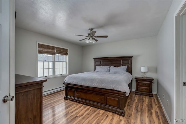 bedroom with a baseboard heating unit, wood finished floors, baseboards, and ceiling fan