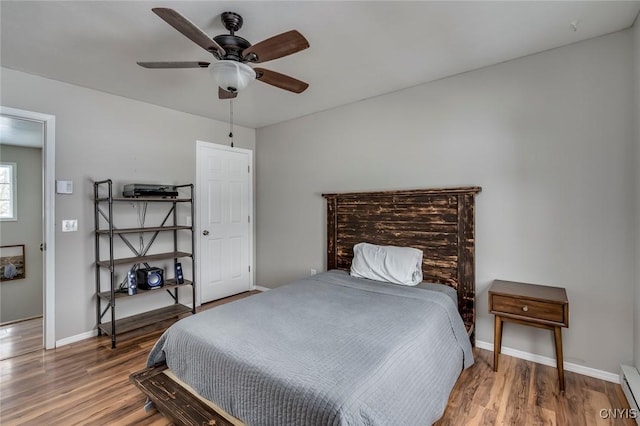 bedroom featuring wood finished floors, baseboards, baseboard heating, and ceiling fan