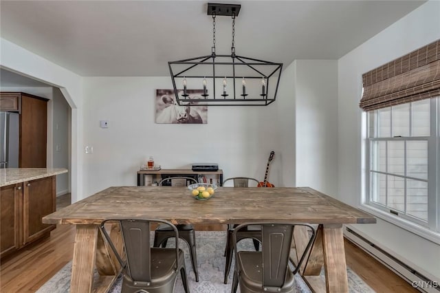 dining room featuring a baseboard heating unit, light wood-style flooring, and arched walkways