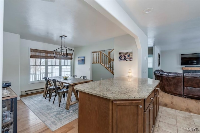 kitchen featuring a center island, decorative light fixtures, open floor plan, light stone counters, and light wood-style floors