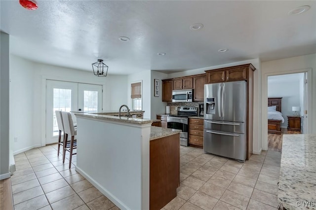 kitchen featuring an island with sink, decorative backsplash, french doors, light tile patterned flooring, and stainless steel appliances