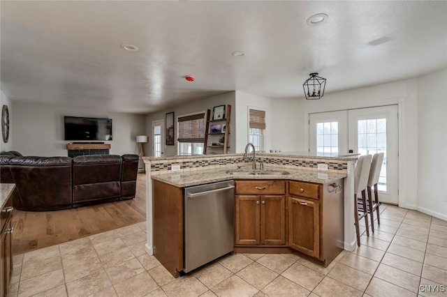 kitchen with a sink, stainless steel dishwasher, open floor plan, brown cabinetry, and light tile patterned floors