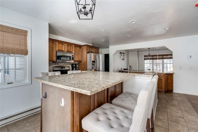 kitchen featuring light stone counters, a baseboard heating unit, backsplash, appliances with stainless steel finishes, and light tile patterned flooring