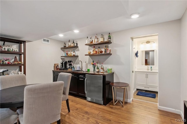 bar with visible vents, light wood-type flooring, indoor wet bar, fridge, and a sink