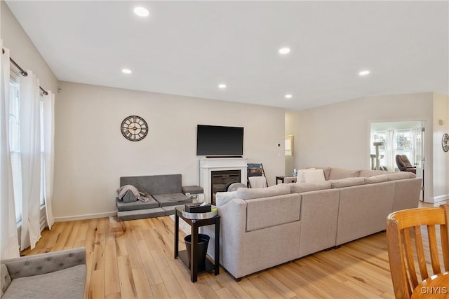 living area featuring recessed lighting, light wood-type flooring, baseboards, and a glass covered fireplace