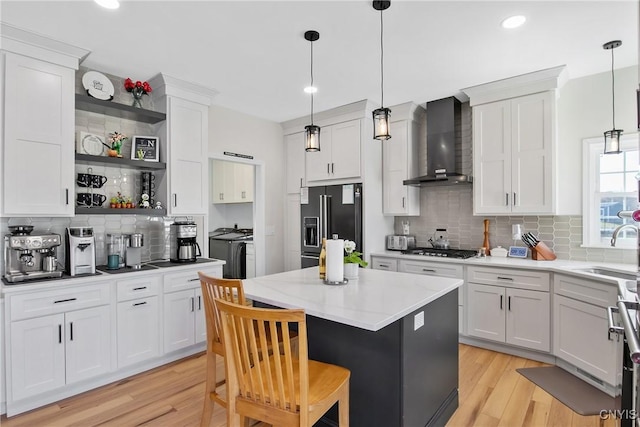 kitchen featuring a kitchen island, black refrigerator with ice dispenser, independent washer and dryer, wall chimney exhaust hood, and a sink