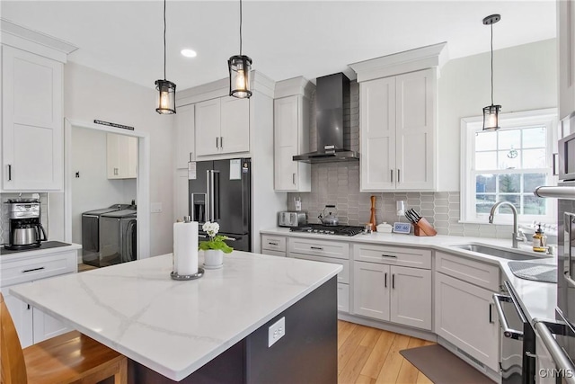 kitchen with separate washer and dryer, a sink, white cabinets, wall chimney range hood, and high end black fridge