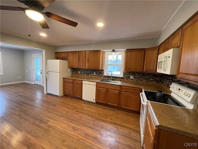 kitchen with backsplash, light wood-type flooring, brown cabinetry, white appliances, and a sink