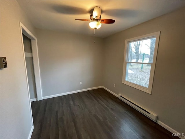 empty room with dark wood finished floors, a ceiling fan, a baseboard heating unit, and baseboards