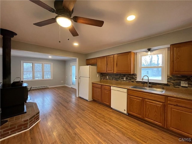 kitchen featuring brown cabinets, a sink, white appliances, light wood finished floors, and a wood stove