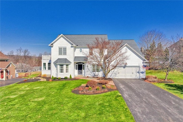 traditional home with aphalt driveway, a balcony, an attached garage, and a front yard