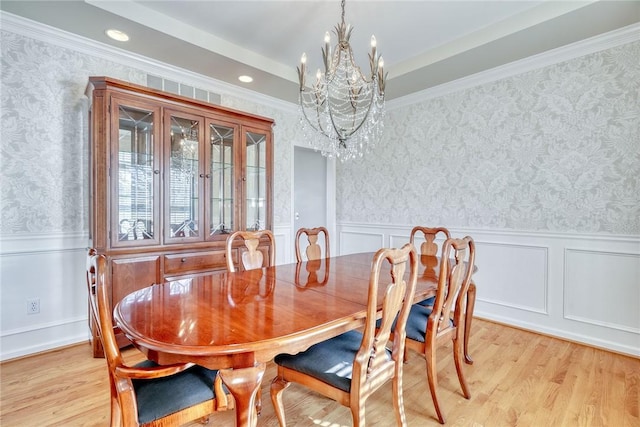 dining space with a notable chandelier, a wainscoted wall, wallpapered walls, and light wood-style floors