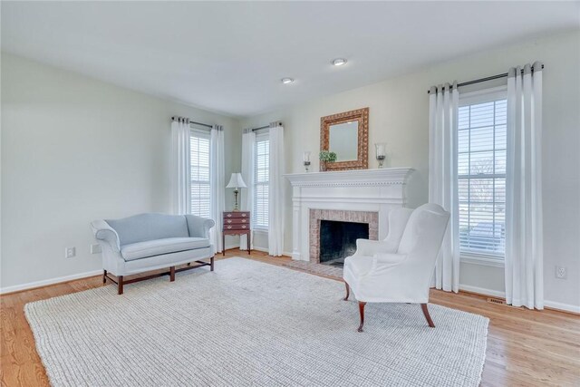 living area featuring a brick fireplace, light wood-style flooring, and baseboards