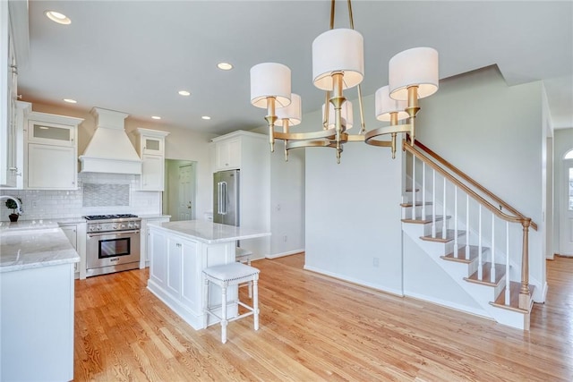 kitchen with light wood finished floors, backsplash, premium range hood, high quality appliances, and white cabinetry