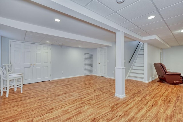 finished below grade area with a drop ceiling, stairway, baseboards, and light wood-style flooring