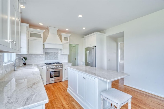 kitchen featuring premium range hood, high quality appliances, a sink, light wood finished floors, and decorative backsplash