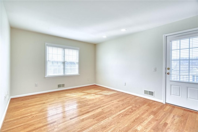 empty room with light wood finished floors, visible vents, and baseboards