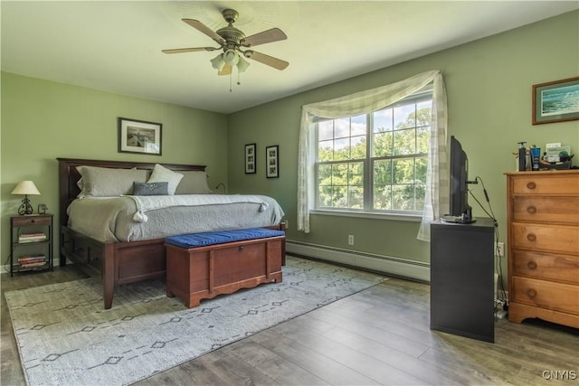 bedroom with baseboards, a baseboard heating unit, a ceiling fan, and wood finished floors